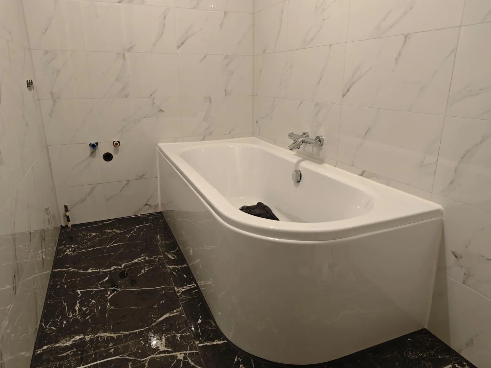 Badewanne mit hellen Wandfliesen und dunklem Boden in Marmoroptik